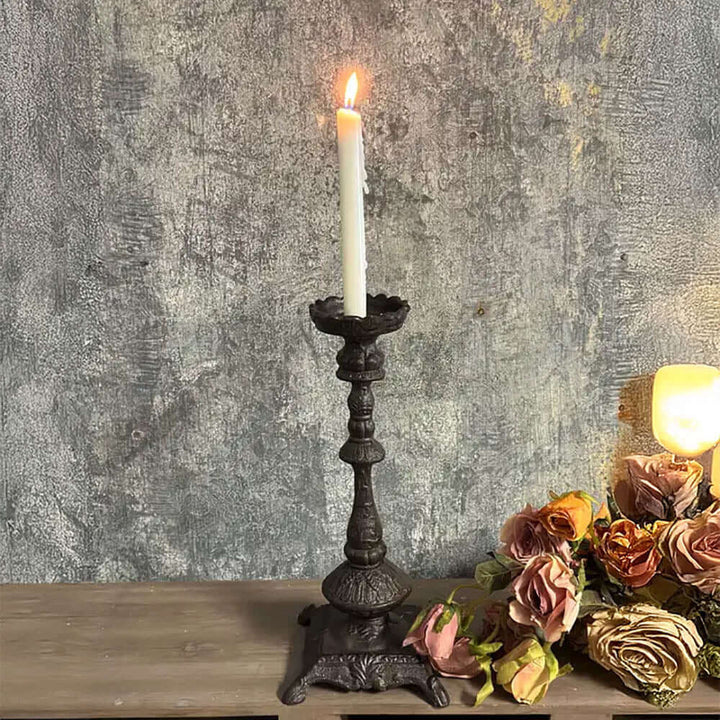 Antique cast iron candle holder with a lit candle, showcasing intricate details and a vintage finish.