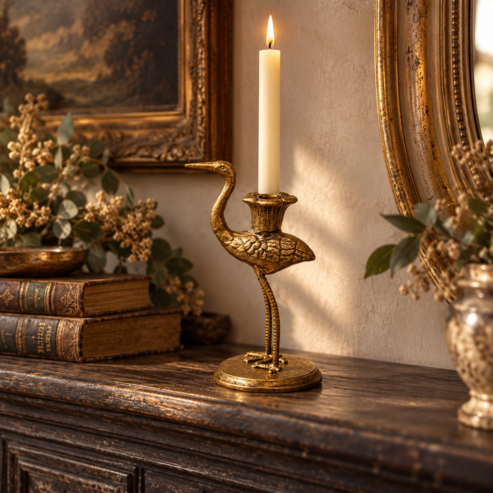 Antique gold crane holder with a lit taper on a dark console