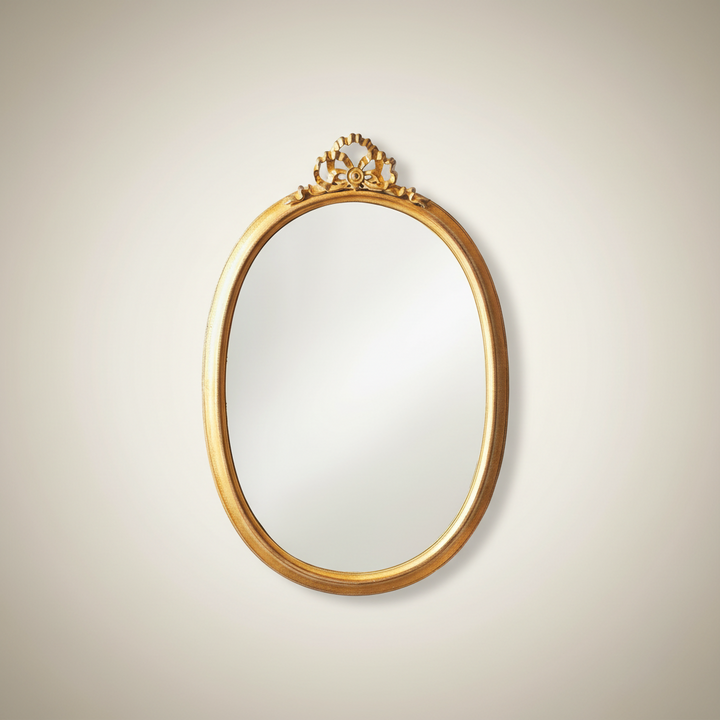 Decorative gold-framed mirror on a beige wall