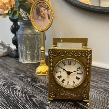 Gold table clock on a wood table beside framed decor
