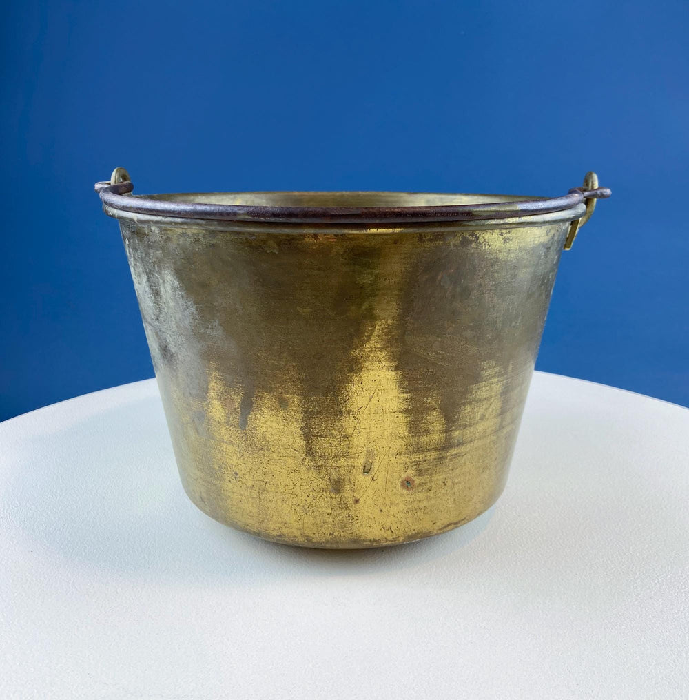 Antique Hand-Hammered Brass Bucket with Wrought Iron Handle: Rustic Farmhouse Decor on a white table with blue background.