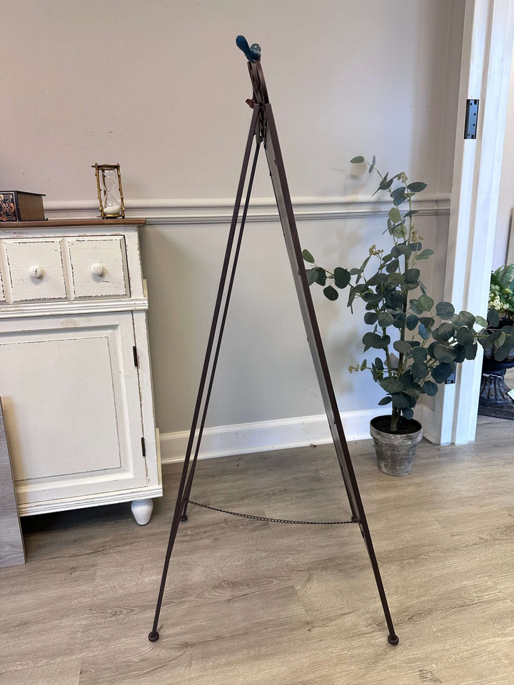 Antique iron chalkboard easel with heart scroll and bird accents in a vintage-themed room.