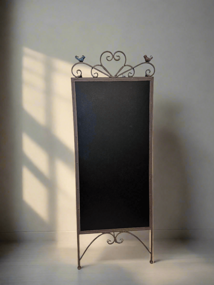 Antique iron chalkboard easel with heart scroll and bird accents, vintage decorative piece with matte black writing surface.