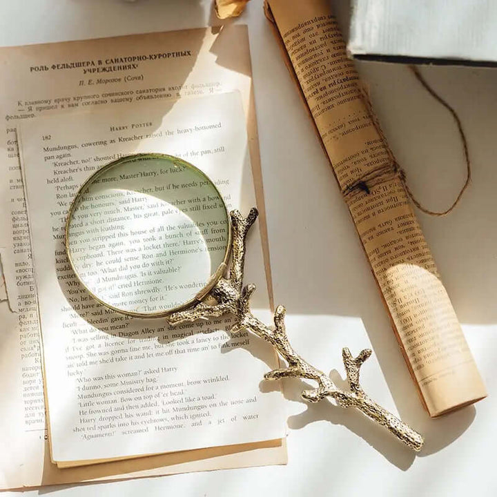 Antique-style gold branch magnifying glass on open book, evoking a vintage, nature-inspired design with a distressed gold finish.