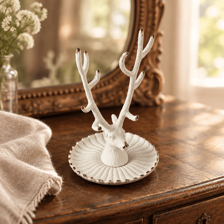 Antique white pewter stag jewelry dish styled on a wooden vanity beside linen and a vintage mirror