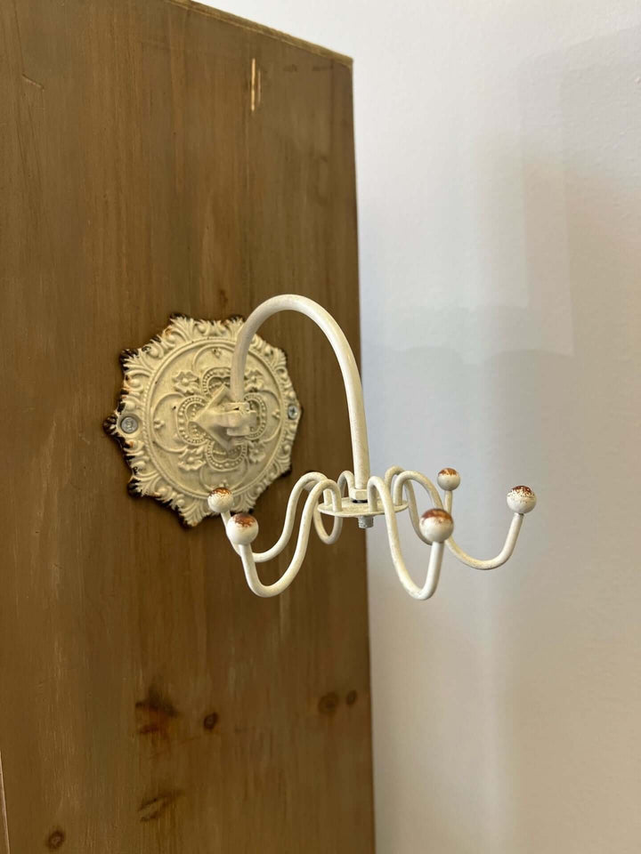 Antique white wall hook with ornate medallion backplate on wooden surface, perfect for vintage decor.