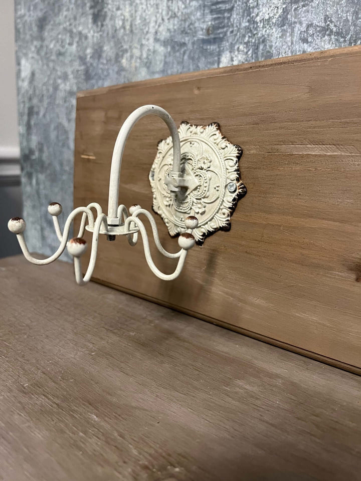 Antique white wall hook with ornate medallion backplate against a wooden background, showcasing vintage charm.