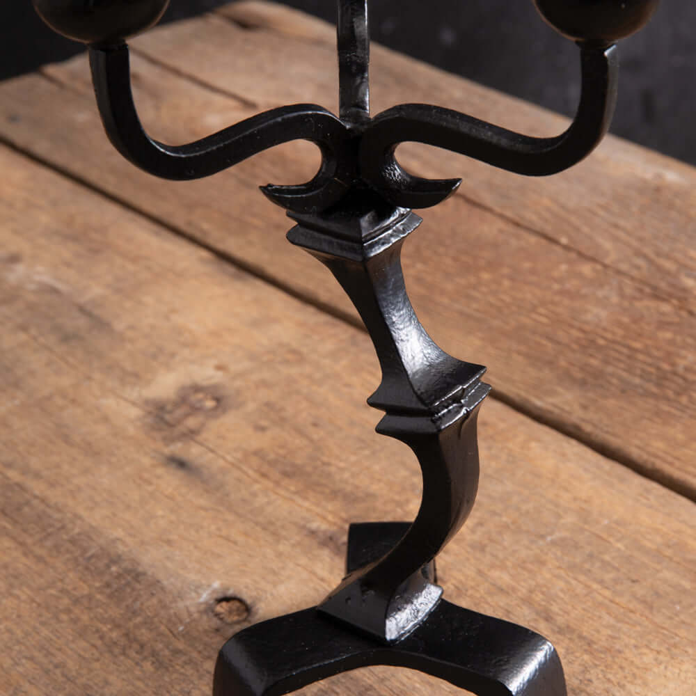 Close-up of antique black iron gothic candelabra on wooden surface, highlighting intricate arm design for Halloween centerpiece.