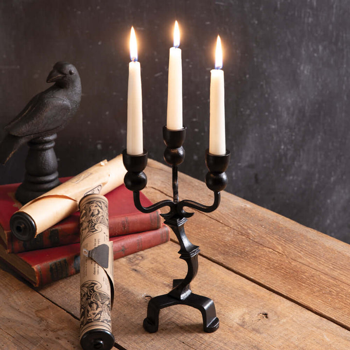 Antique black iron Gothic candelabra with candles, perfect for a Halloween centerpiece, on rustic wood table with vintage decorations.