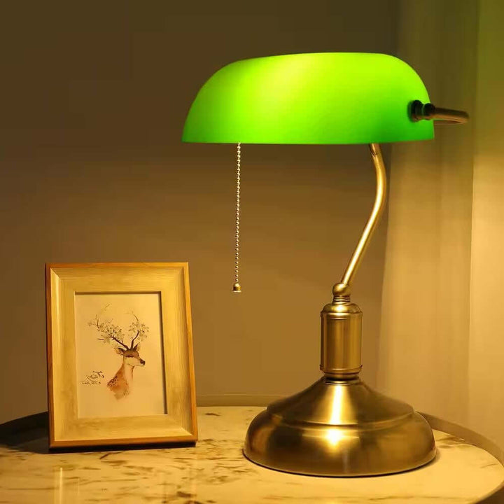 Antique Brass Bankers Lamp with Green Glass Shade on a marble table next to a framed deer sketch.