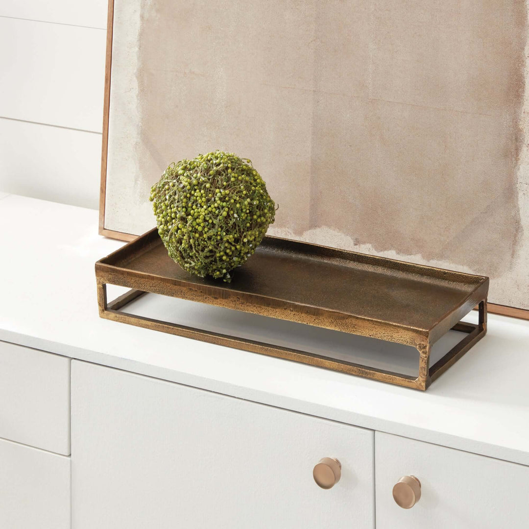 Antique brass raised tray displaying greenery, combines vintage charm and modern elegance on a white shelf.
