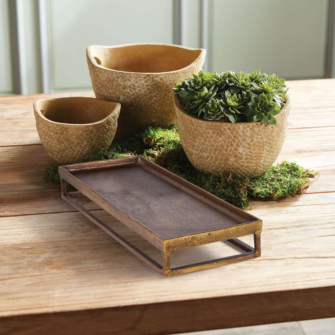 Antique brass raised display tray on rustic table, showcasing elegance and vintage charm with a touch of greenery.
