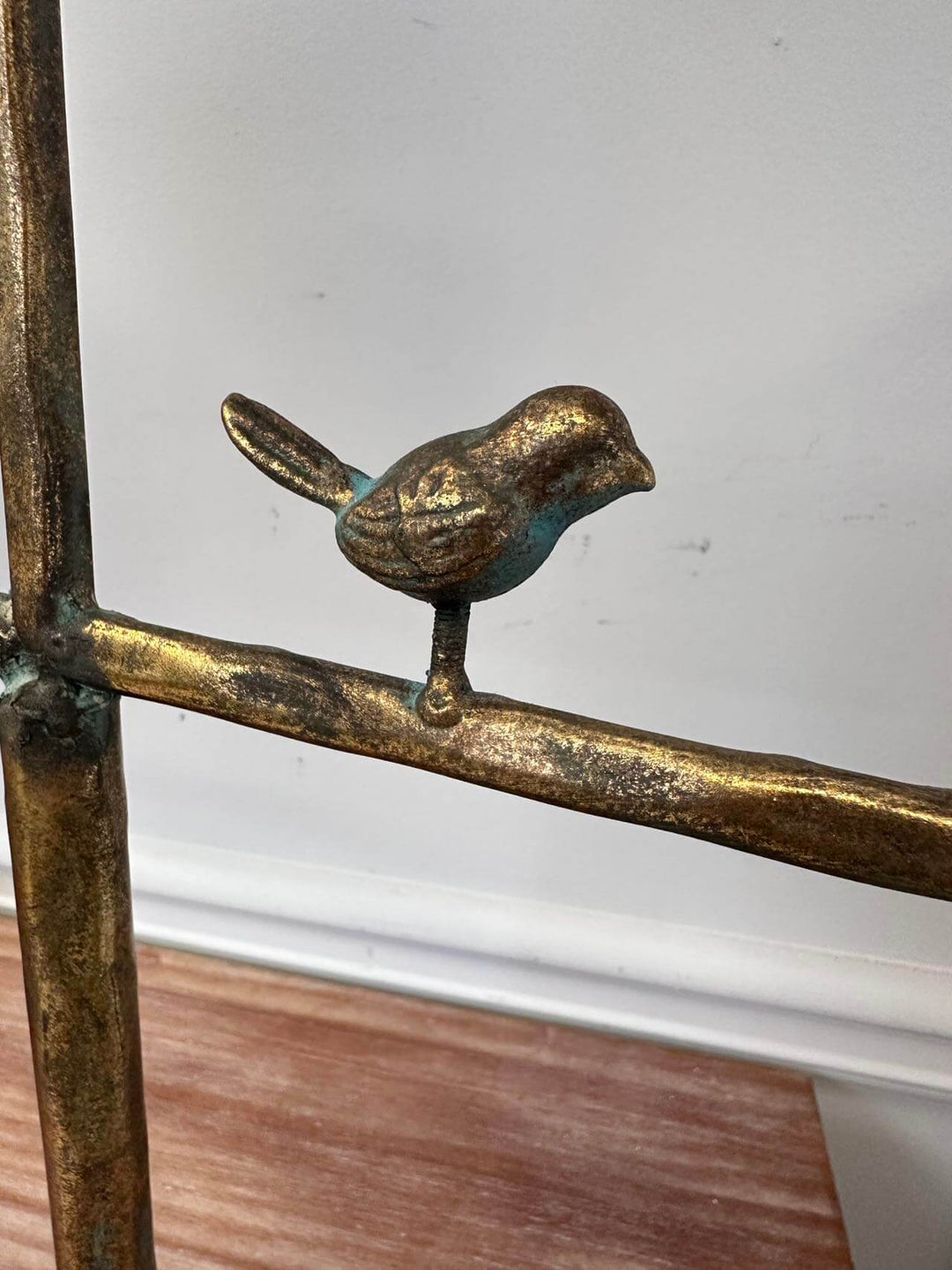 Bronze bird sculpture perched on a metallic branch against a neutral background.