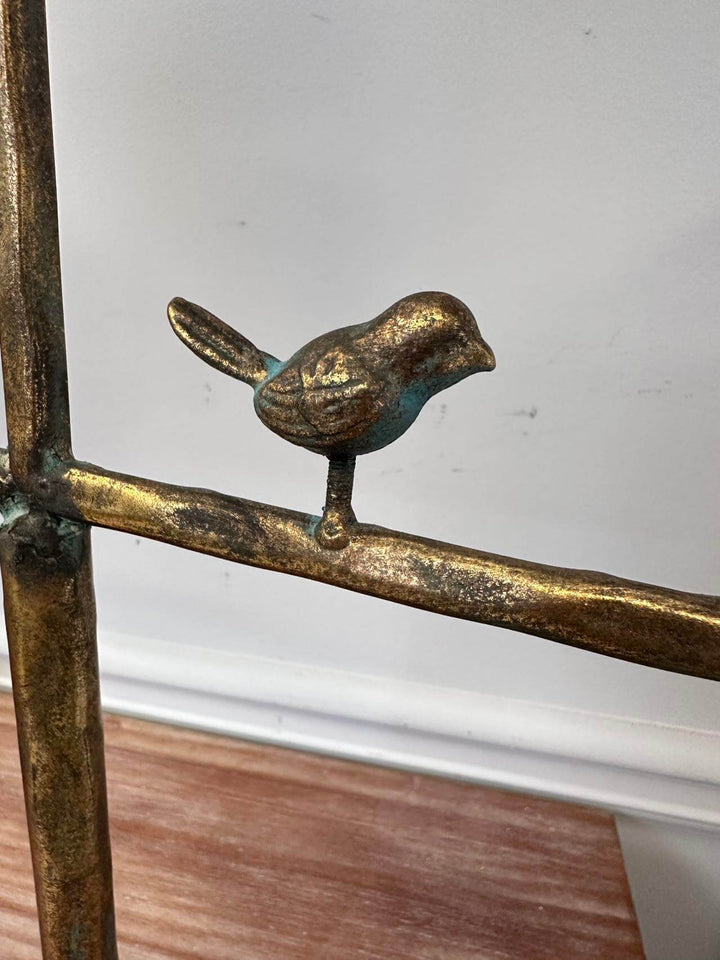 Bronze bird sculpture perched on a metallic branch against a neutral background.