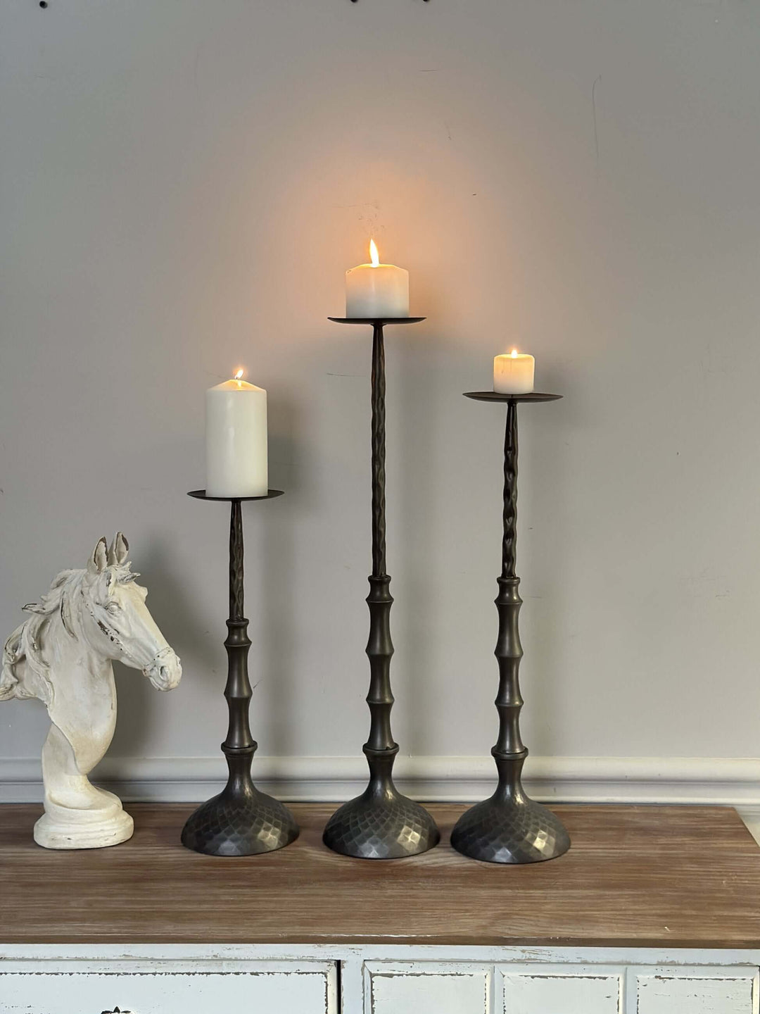 Antique bronze hammered metal candle holders with lit pillar candles on wooden surface.