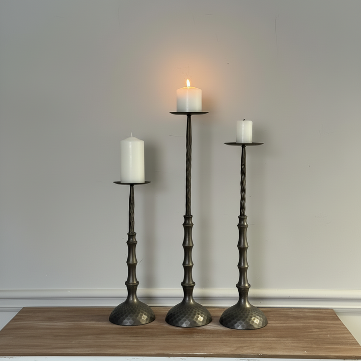 Three candle holders with candles on a wooden surface against a plain wall.