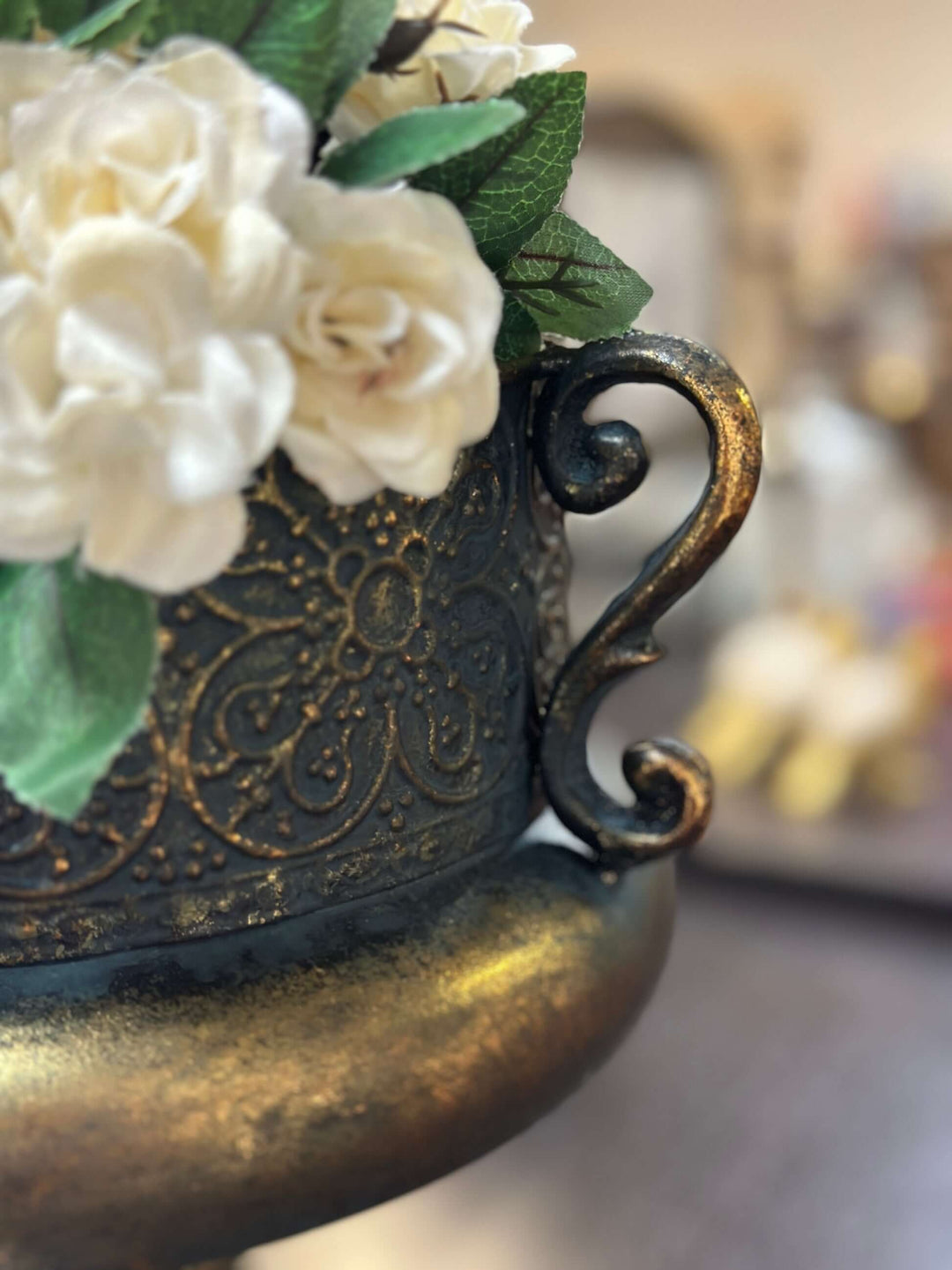 Close-up of an ornate antique bronze metal urn with floral detailing and hand-rubbed gold highlights.
