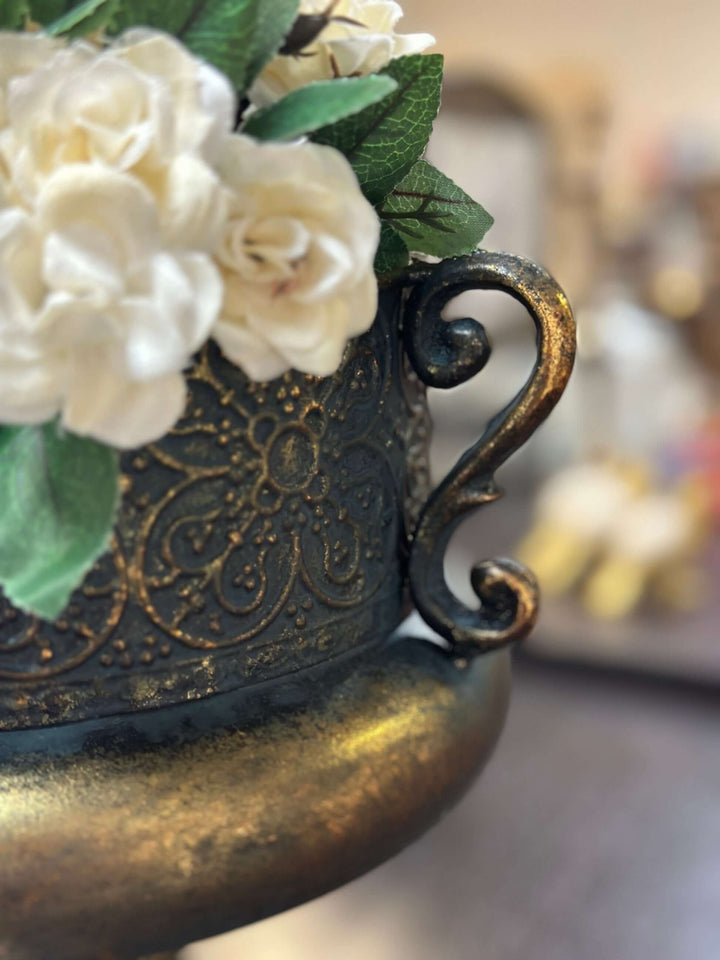 Close-up of an ornate antique bronze metal urn with floral detailing and hand-rubbed gold highlights.