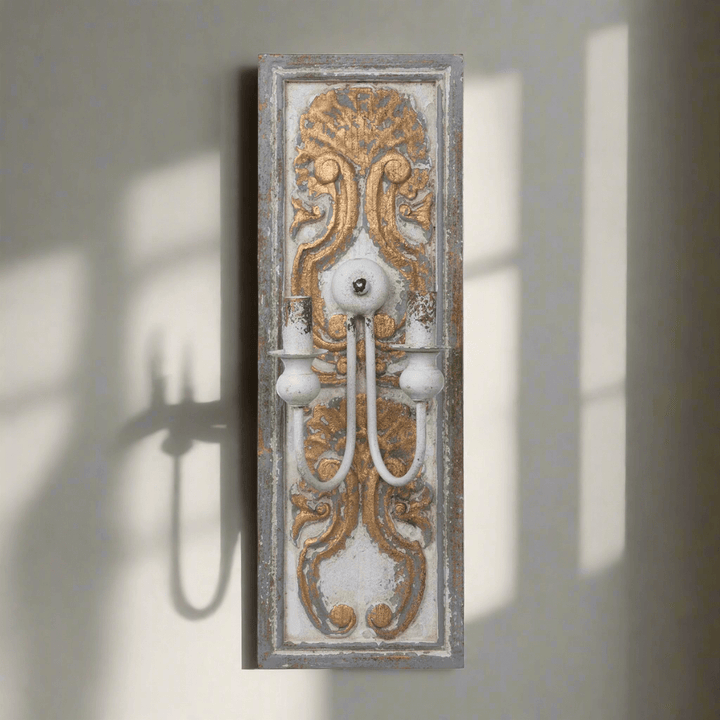 Antique French Country Wall Sconce Light with carved wooden backplate and ornate gold-white finish casting shadow on wall.