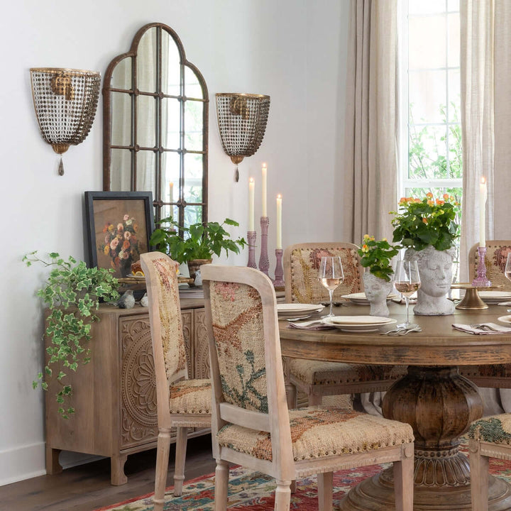 Dining room with antique gold crystal wall sconces, vintage decor, ornate mirror, and rustic dining table setup.