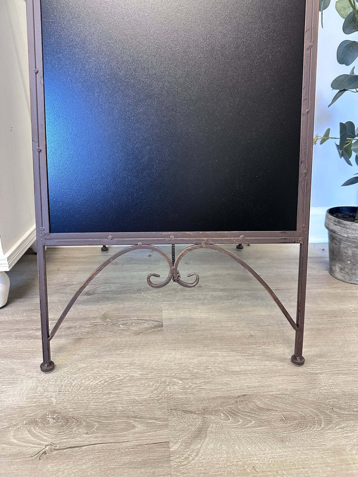 Antique iron chalkboard easel with intricate scrollwork and bird accents, perfect for vintage décor and nostalgic messages.