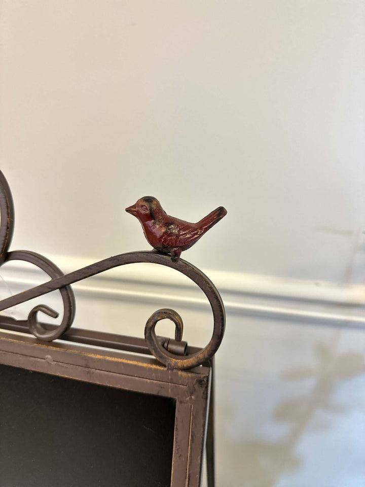 Close-up of antique iron chalkboard easel with bird accent and heart scroll design