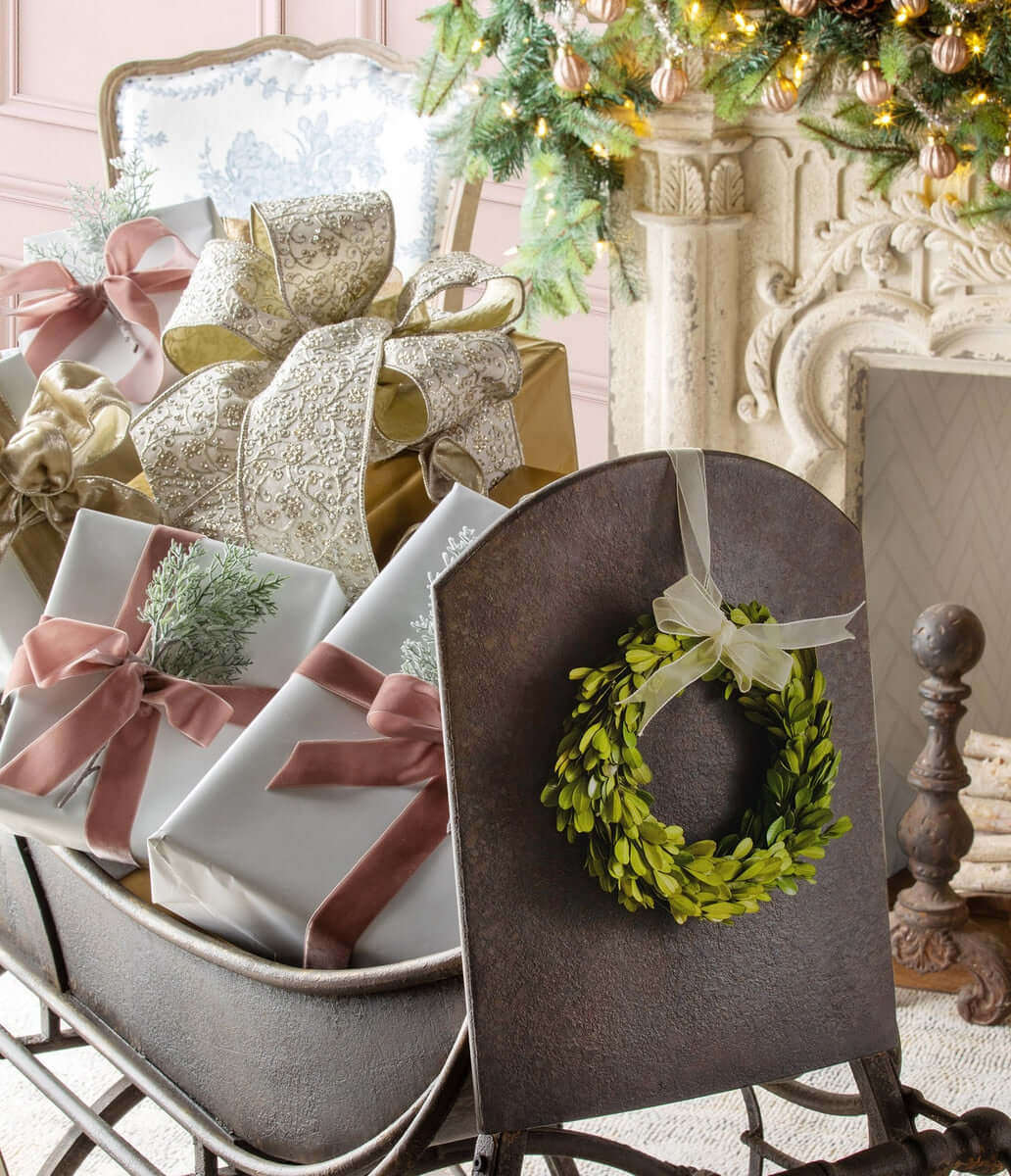 Antique Iron Cutter Sleigh Christmas Décor with wreath and wrapped gifts beside a fireplace and Christmas tree.