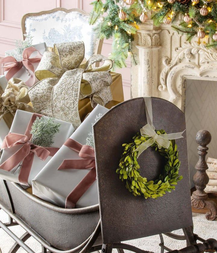 Antique Iron Cutter Sleigh Christmas Décor with wreath and wrapped gifts beside a fireplace and Christmas tree.