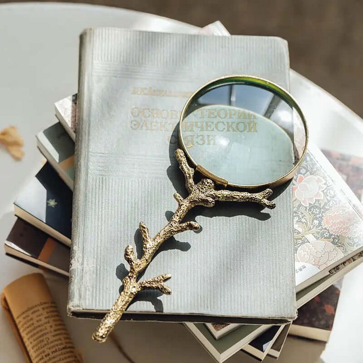 Antique-style gold branch magnifying glass on vintage books, evoking nostalgic charm and beauty.