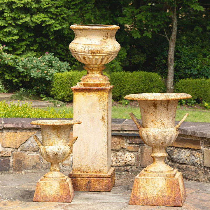 Antique-style iron garden urn with tall pedestal featuring aged patina, enhancing outdoor spaces with vintage European charm.