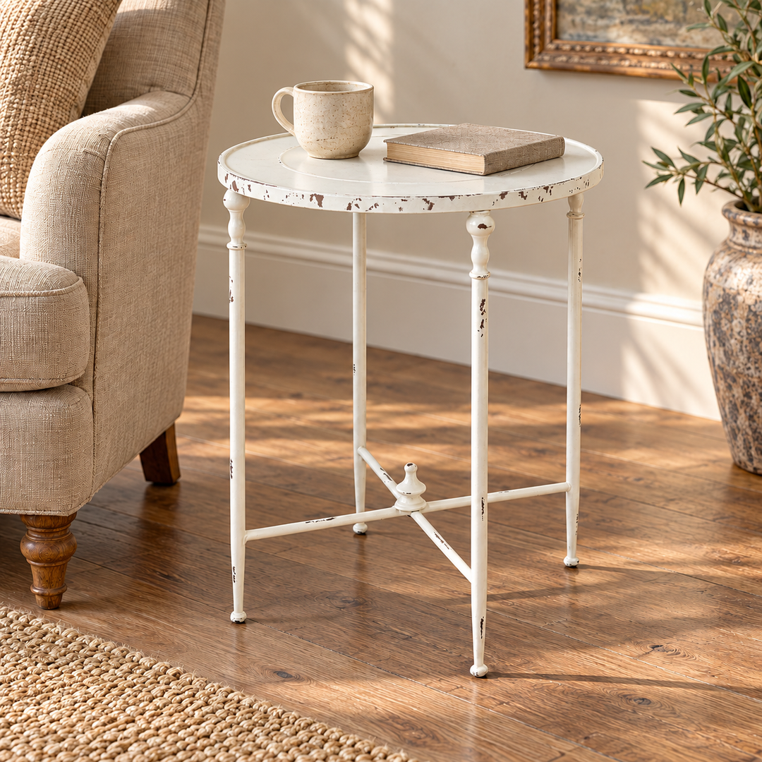 Scene of the Antiqued White Iron Round Side Table beside a linen armchair, with a book and mug.
