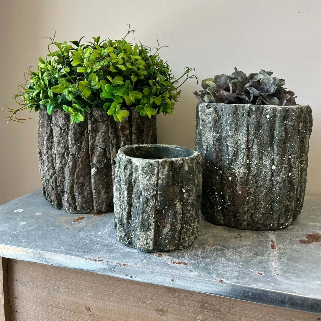 Three dark bark-textured planters on a zinc-topped cabinet