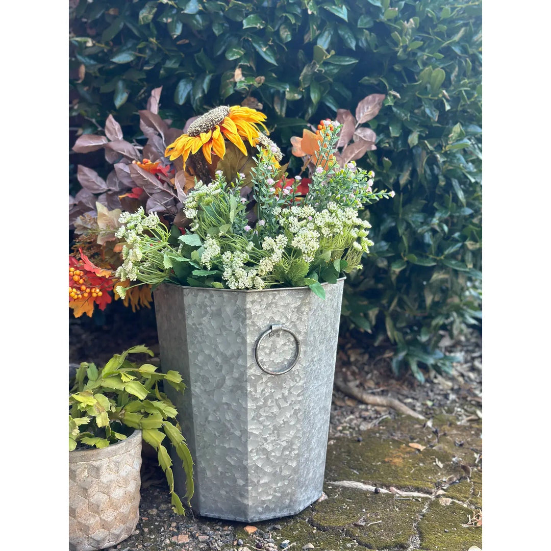 Tall zinc planter with ring handle holding a colorful floral arrangement