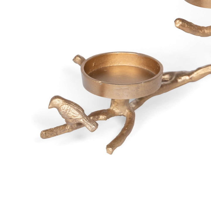 Soft gold candle holder shaped like a branch with a bird, designed for three pillar candles, embodying nature-inspired elegance.