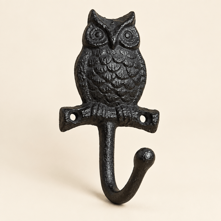 Black cast iron owl wall hook with sculpted feathers and a curved hook on an ivory background