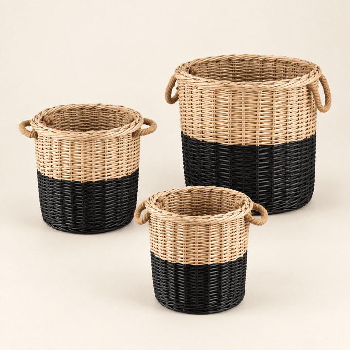 Three round willow storage baskets with natural upper sections, black-dipped bases, and rope handles on an ivory background.