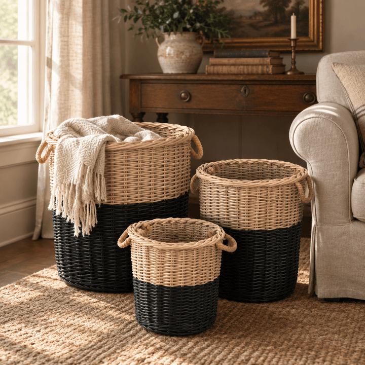 Black-dipped willow basket set styled beside a linen armchair, with a cream throw in the largest basket.