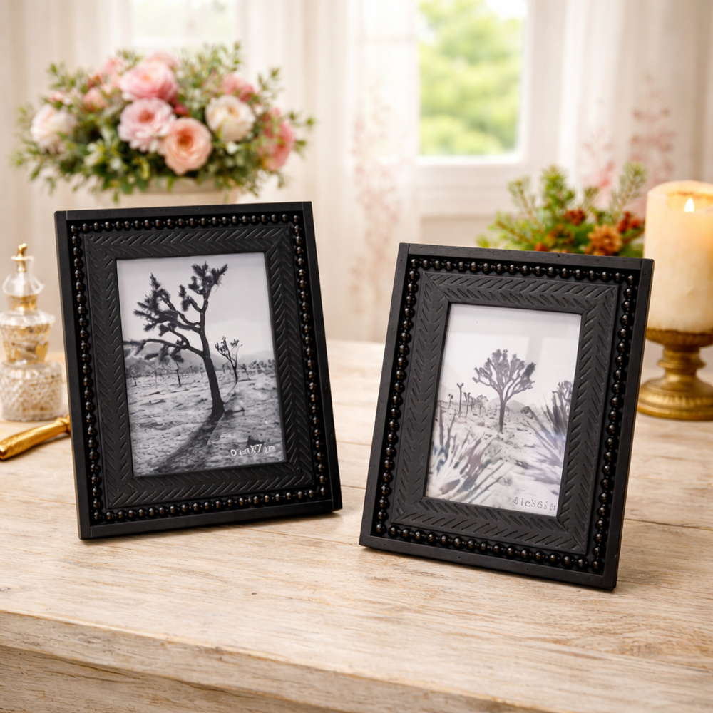 Two black beaded picture frames styled with flowers and candlelight