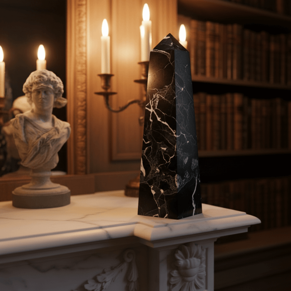Decorative black marble obelisk on a mantel with candles and a bust in the background.