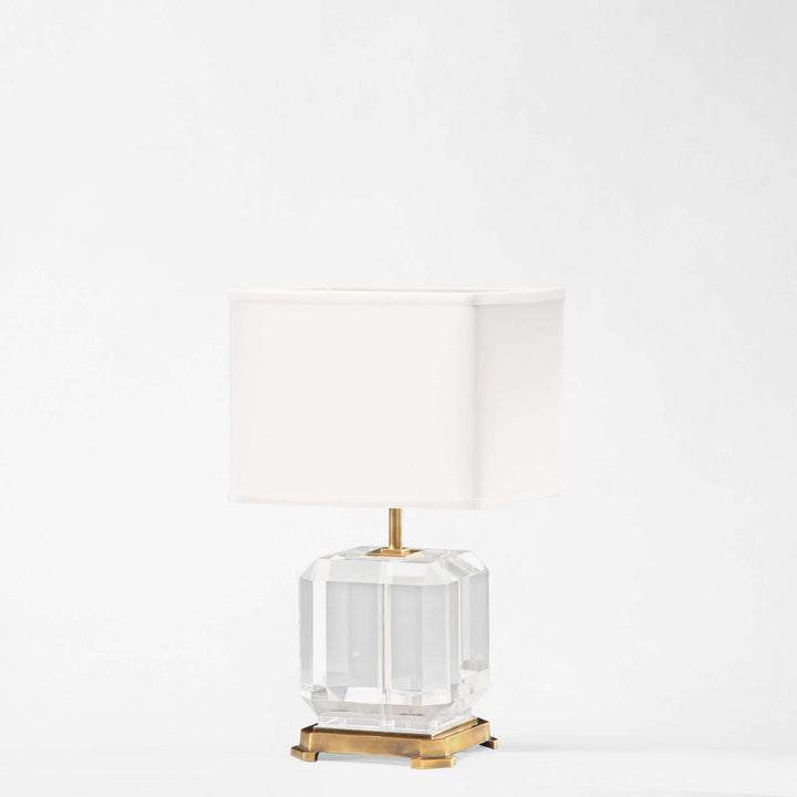 Clear glass table lamp with gold base on a white background