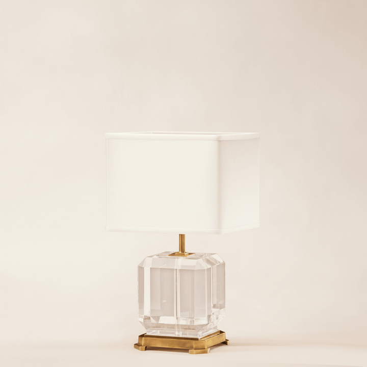 Decorative table lamp with a clear glass base and gold accents on a beige background