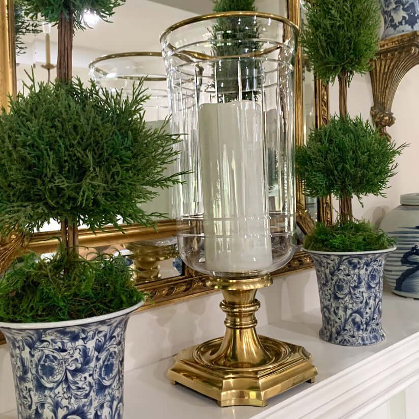 Decorative setup with a gold candle holder, white candle, and potted plants on a surface.