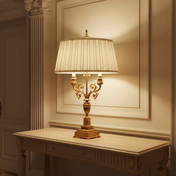 Decorative table lamp with a white shade on a wooden table against a wall with molding.