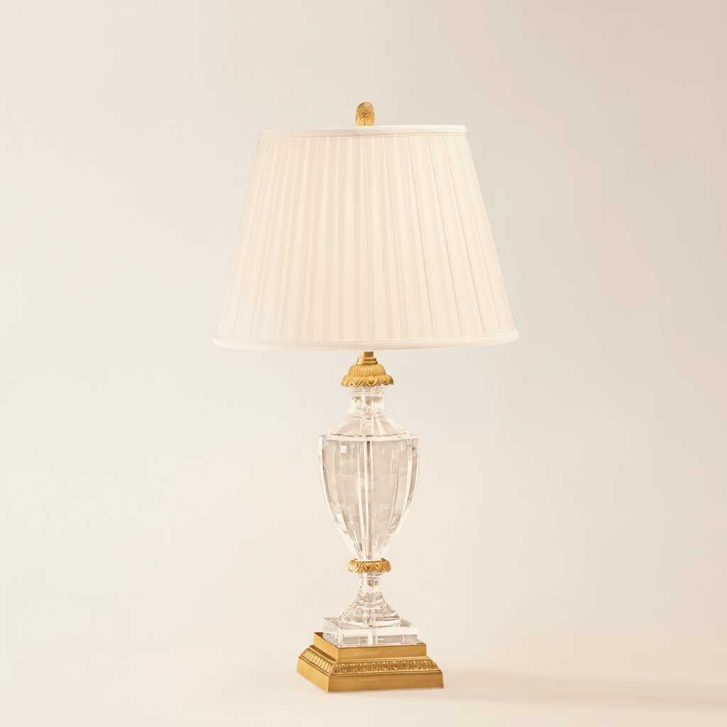 Decorative table lamp with clear glass base and pleated white shade on a beige background