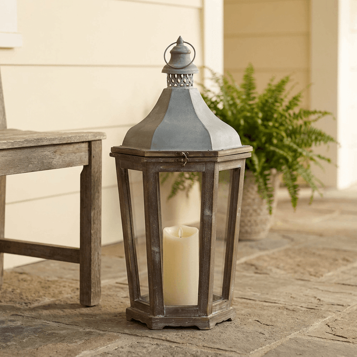 Medium Briarwick Carriage Lantern with an ivory pillar candle on a covered stone porch beside a wood bench