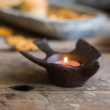 Cast iron bird tea light holder glowing on a rustic wooden table