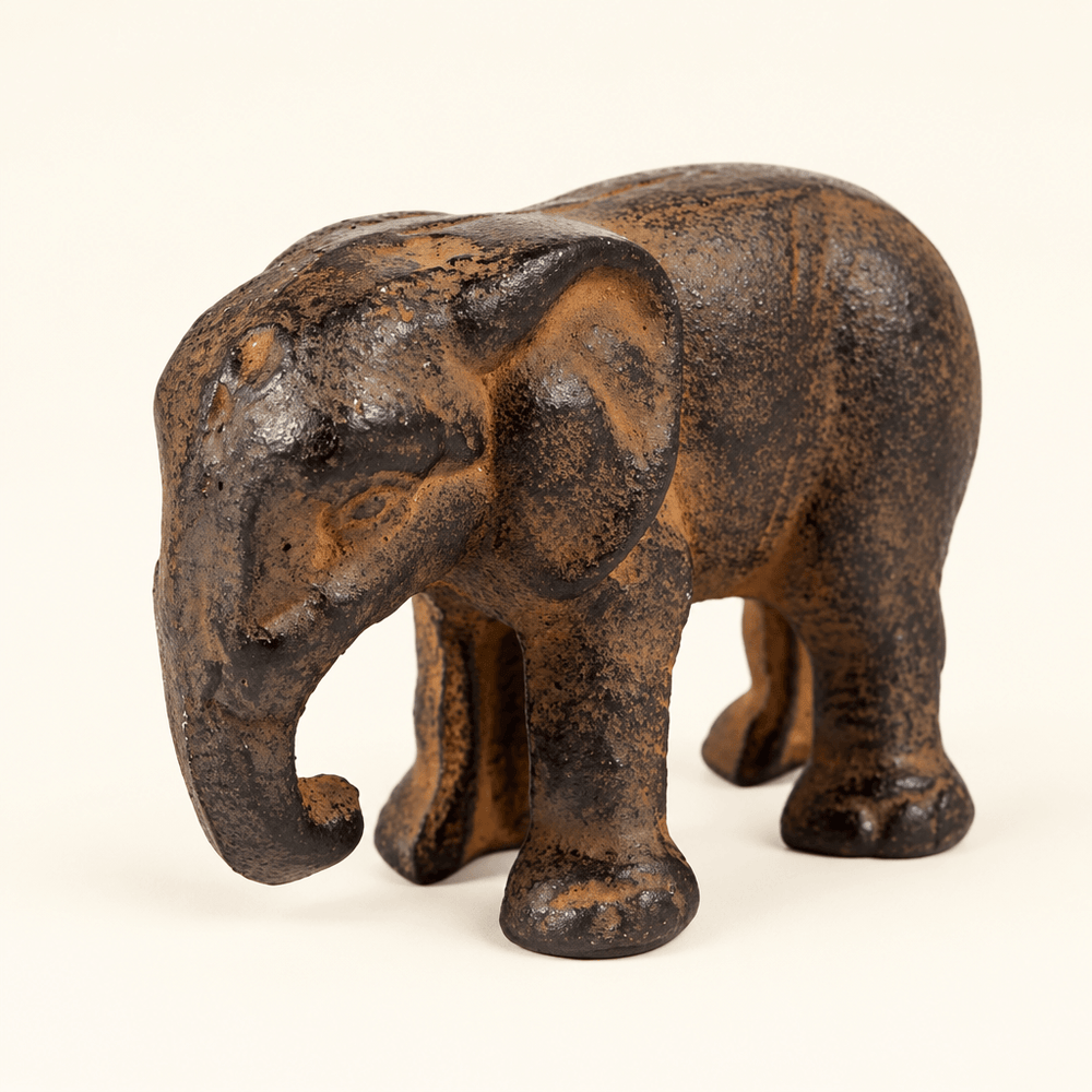 Small dark cast iron elephant figurine with a curled downward trunk on an ivory background.