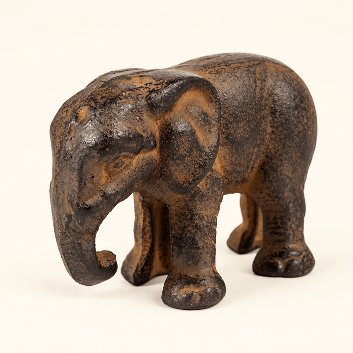Small dark cast iron elephant figurine with a curled downward trunk on an ivory background.