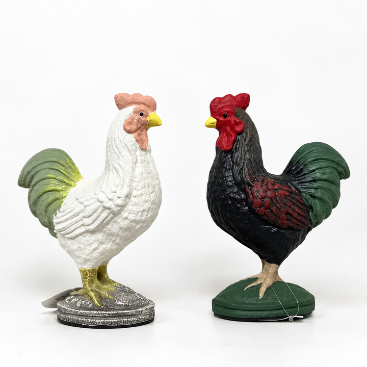 White and green cast iron rooster figurines on a plain background