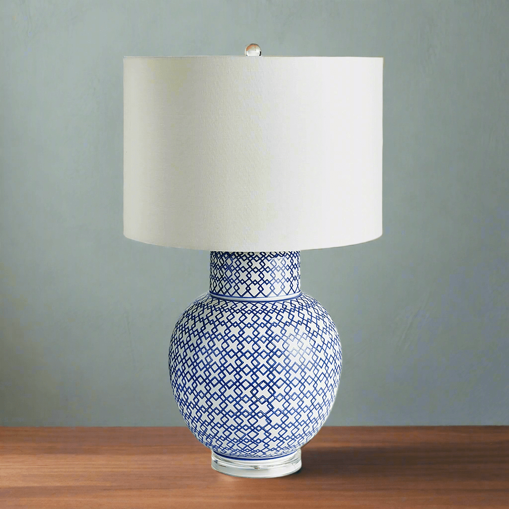 Chinoiserie blue and white ginger jar lamp with a round base and white shade on a wooden table.